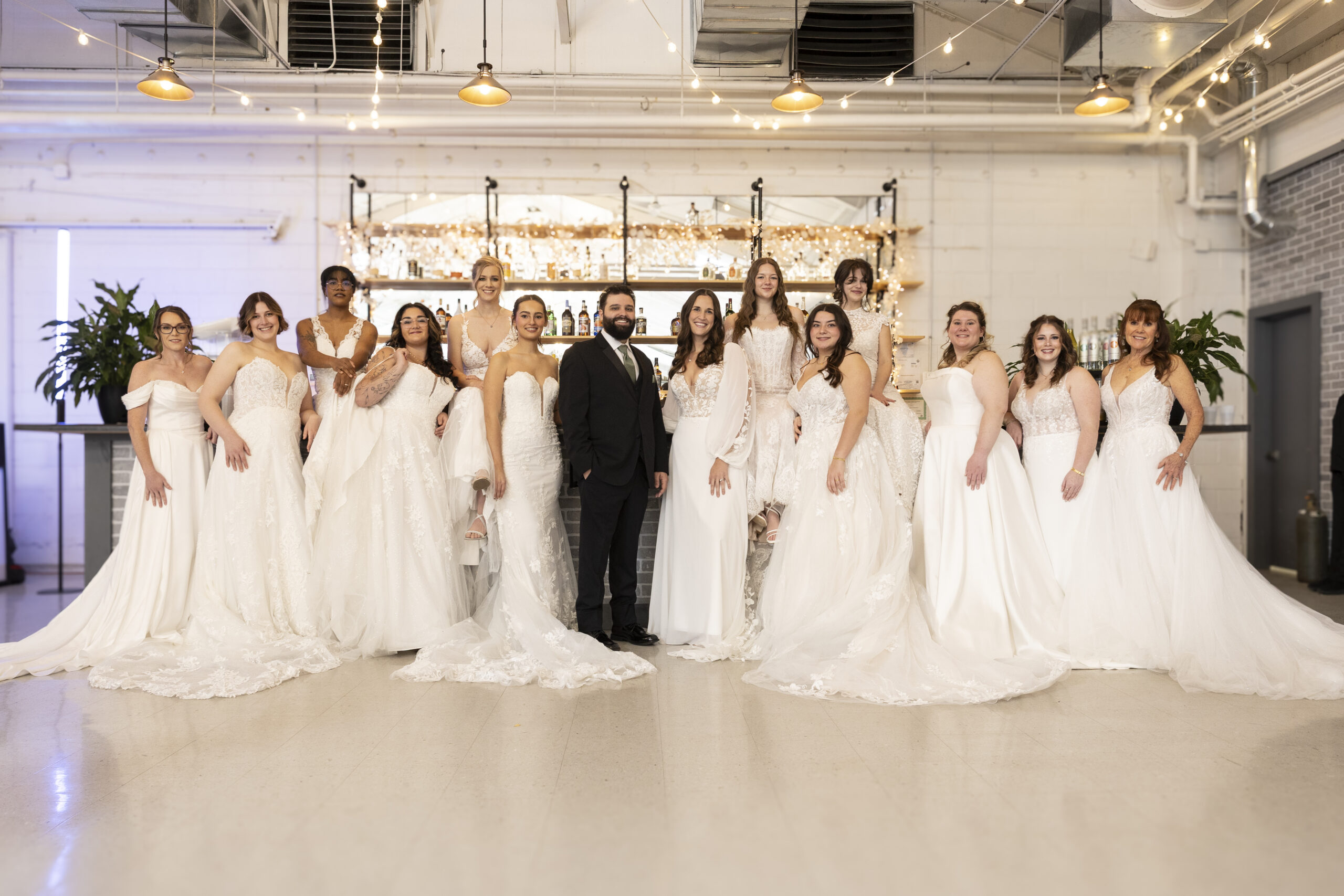 Elegant Brides wearing several styles of dresses with a man in a tuxedo in the center.