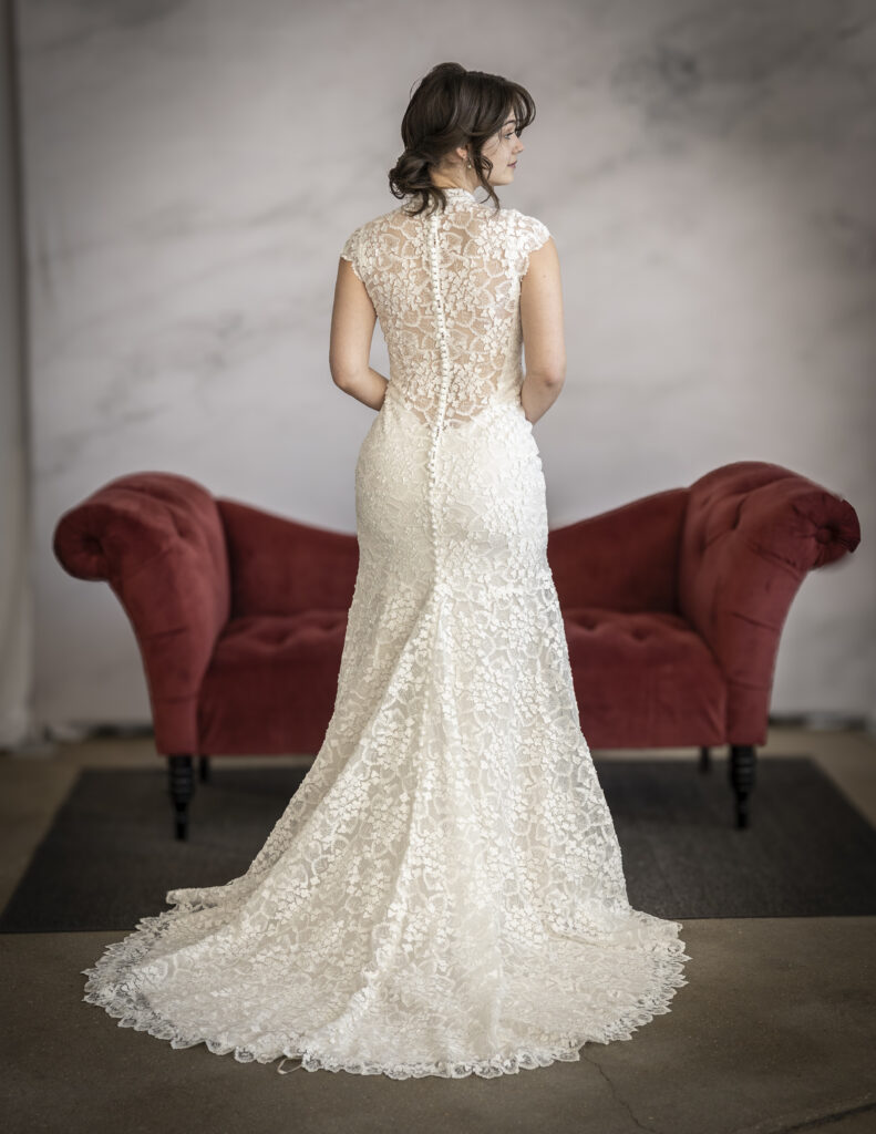 An Elegant Bride Wearing Maggie Sottero's Auburn lace wedding dress, which features intricate lace details, buttons down the back, a high neckline, and an illusion back.