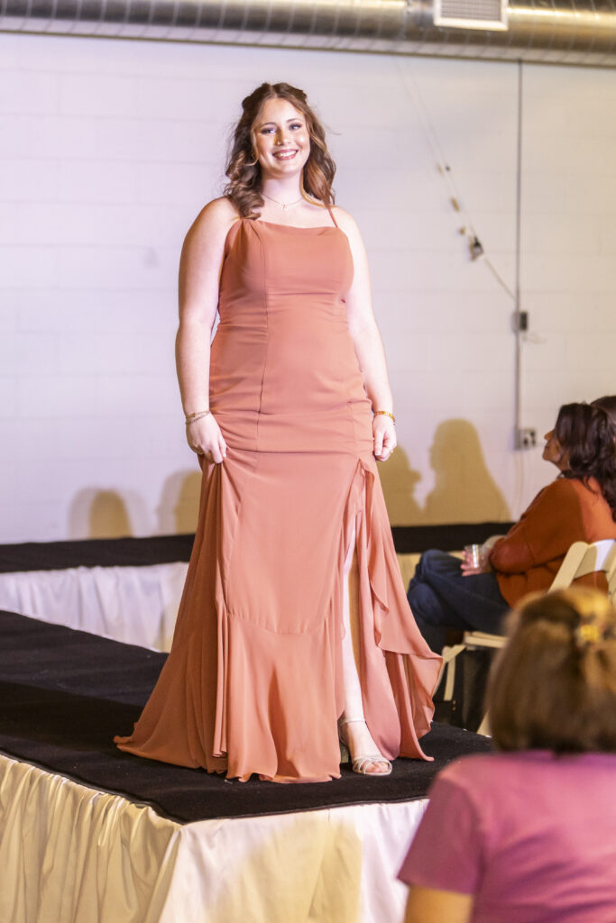 A model wearing an orange morilee bridesmaid dress from Elegant brides.