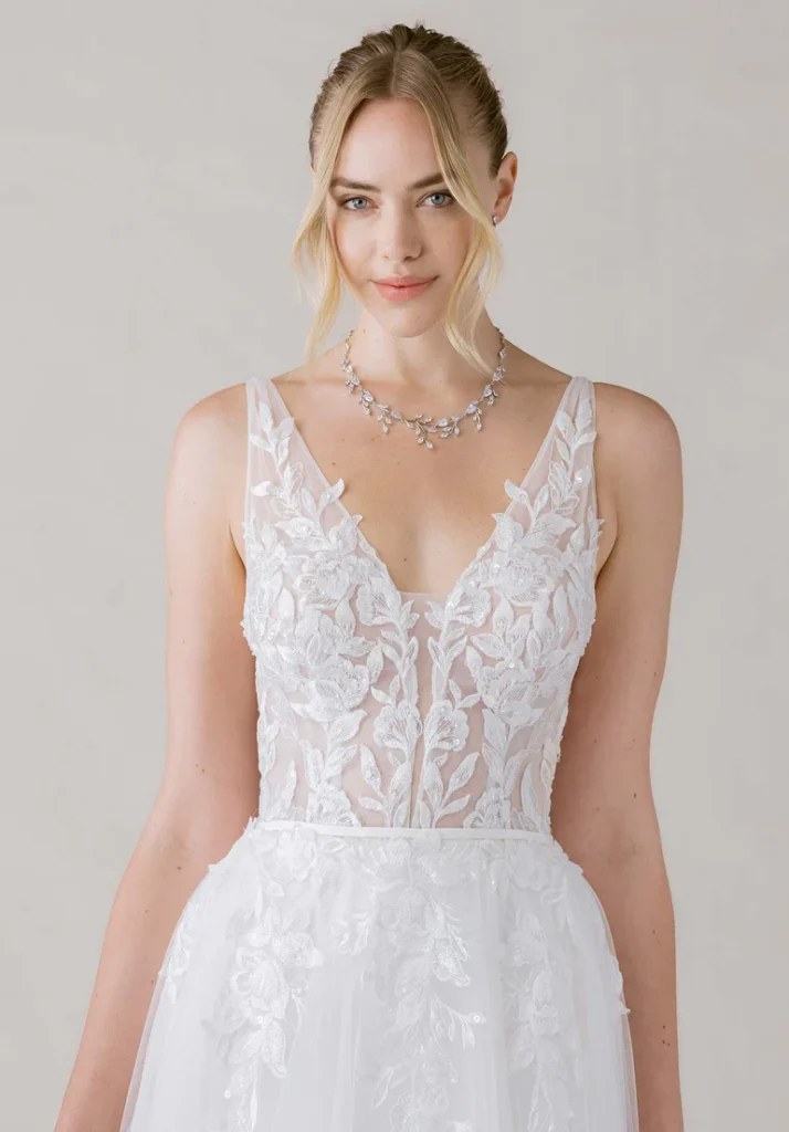 Morilee's Odile wedding dress, featuring a see-through bodice covered in floral lace appliques, a plunging neckline, and lace appliques flowing down the skirt.