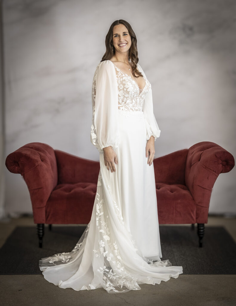 An elegant bride wearing Rebecca Ingram's Sue wedding dress, which features detachable sleeves and peek-a-boo lace appliques in the train.